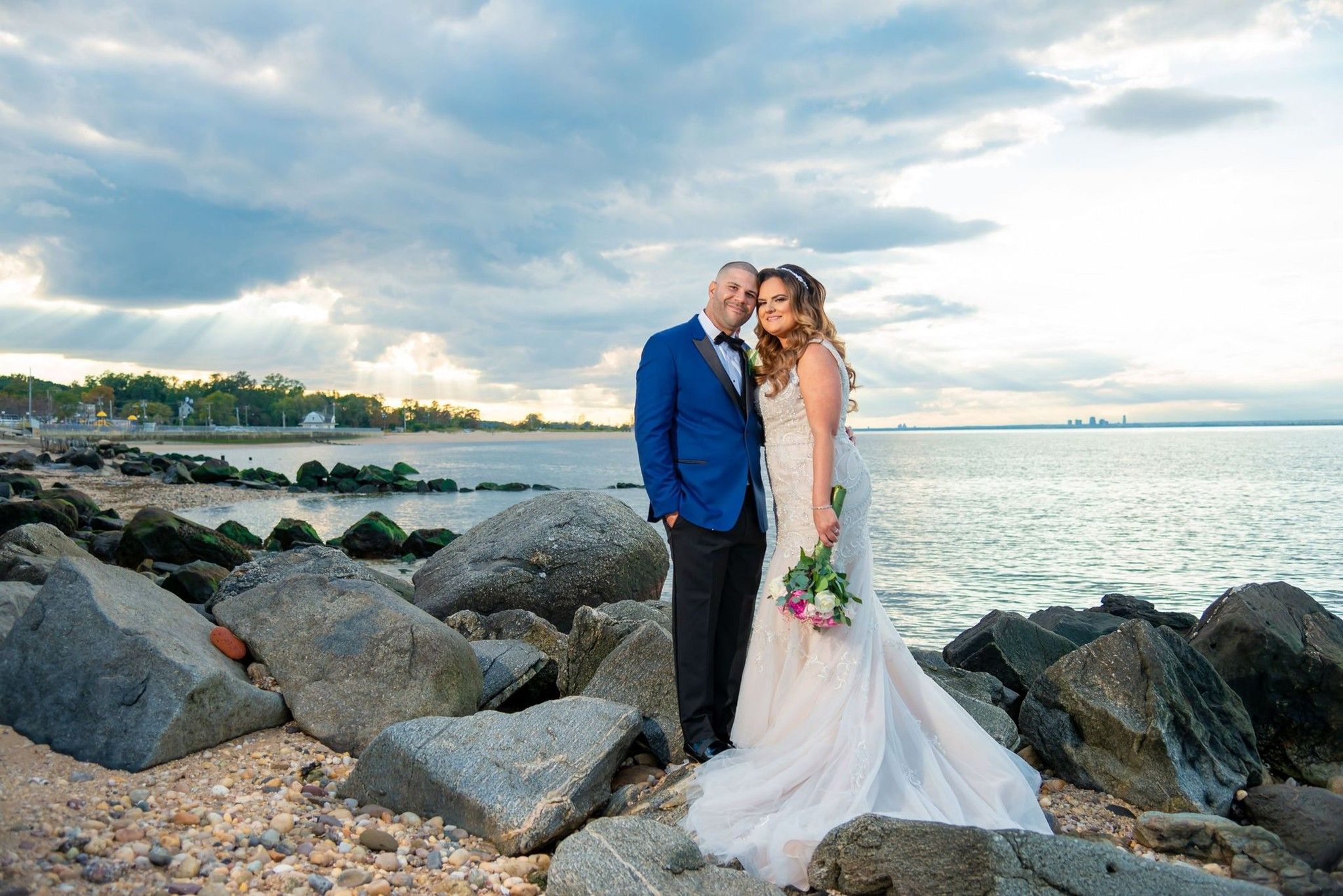 Bride and groom standing among rocks along a cloudy shoreline