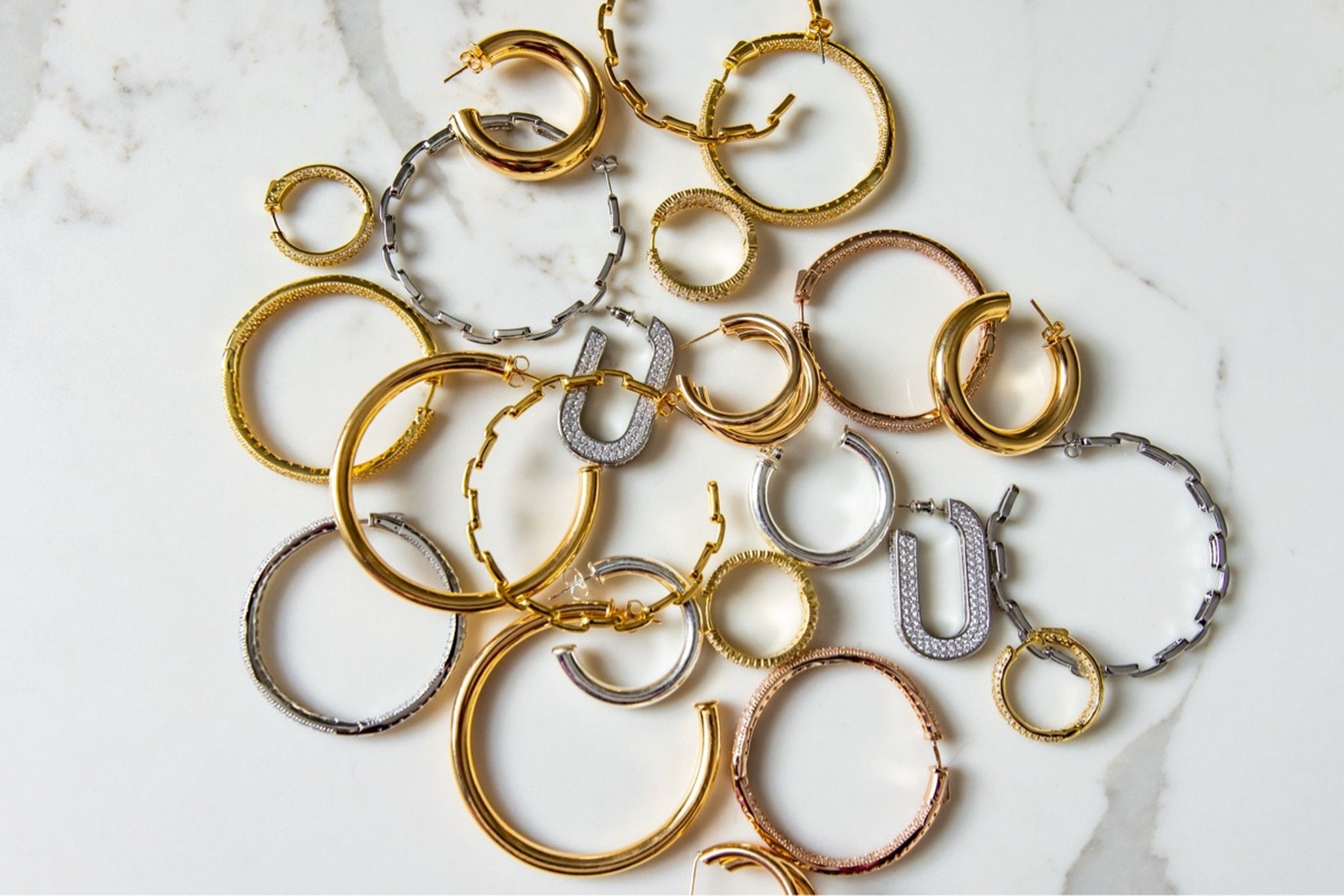 Flat-lay of gold and silver hoop earrings and bangles on marble