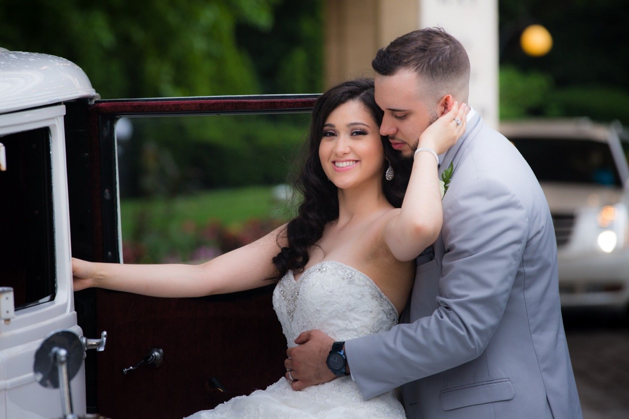 Bride and groom embracing beside a vintage car