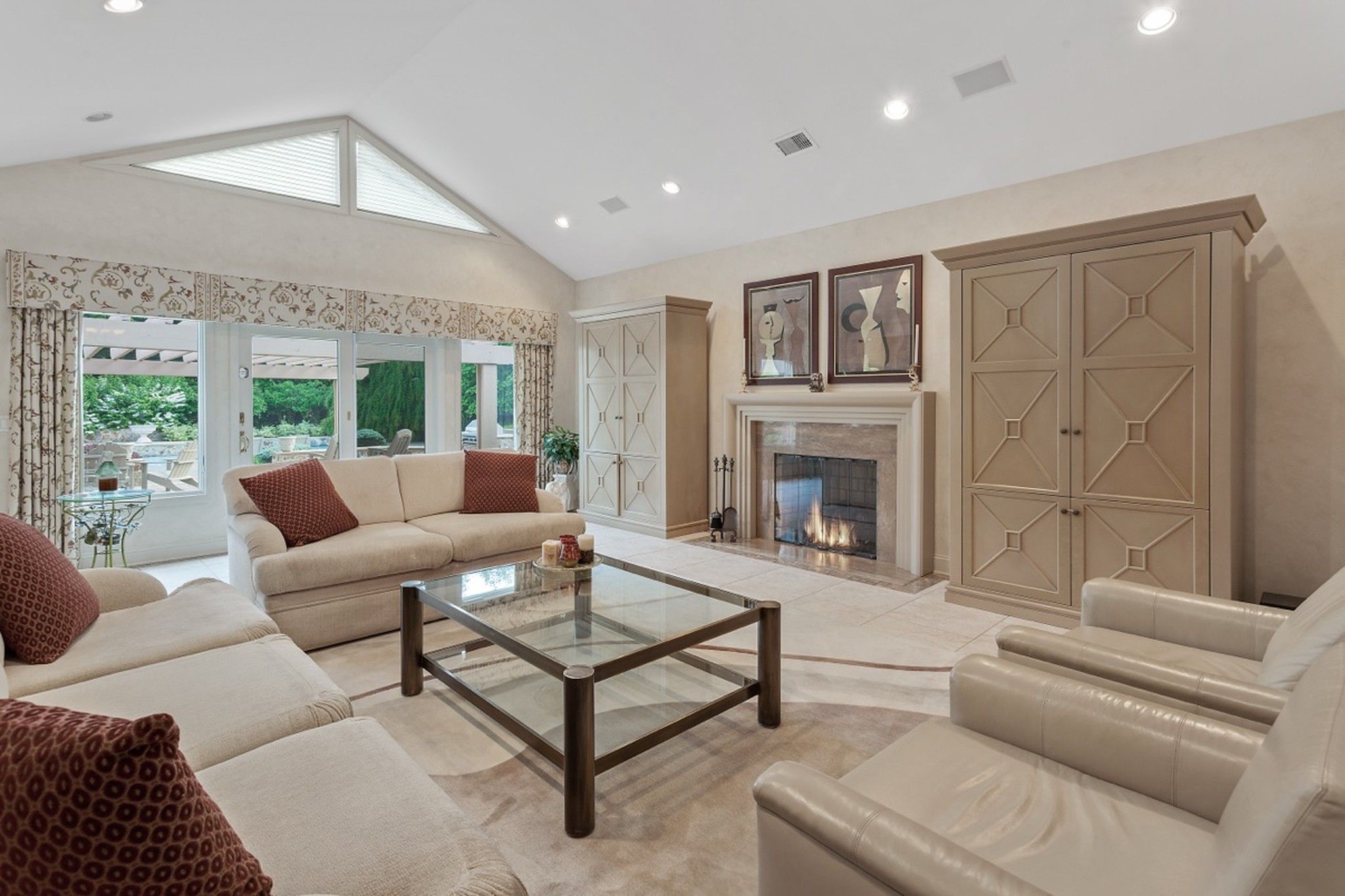 Living room with a lit fireplace, cream sofas, a glass coffee table and garden-view doors