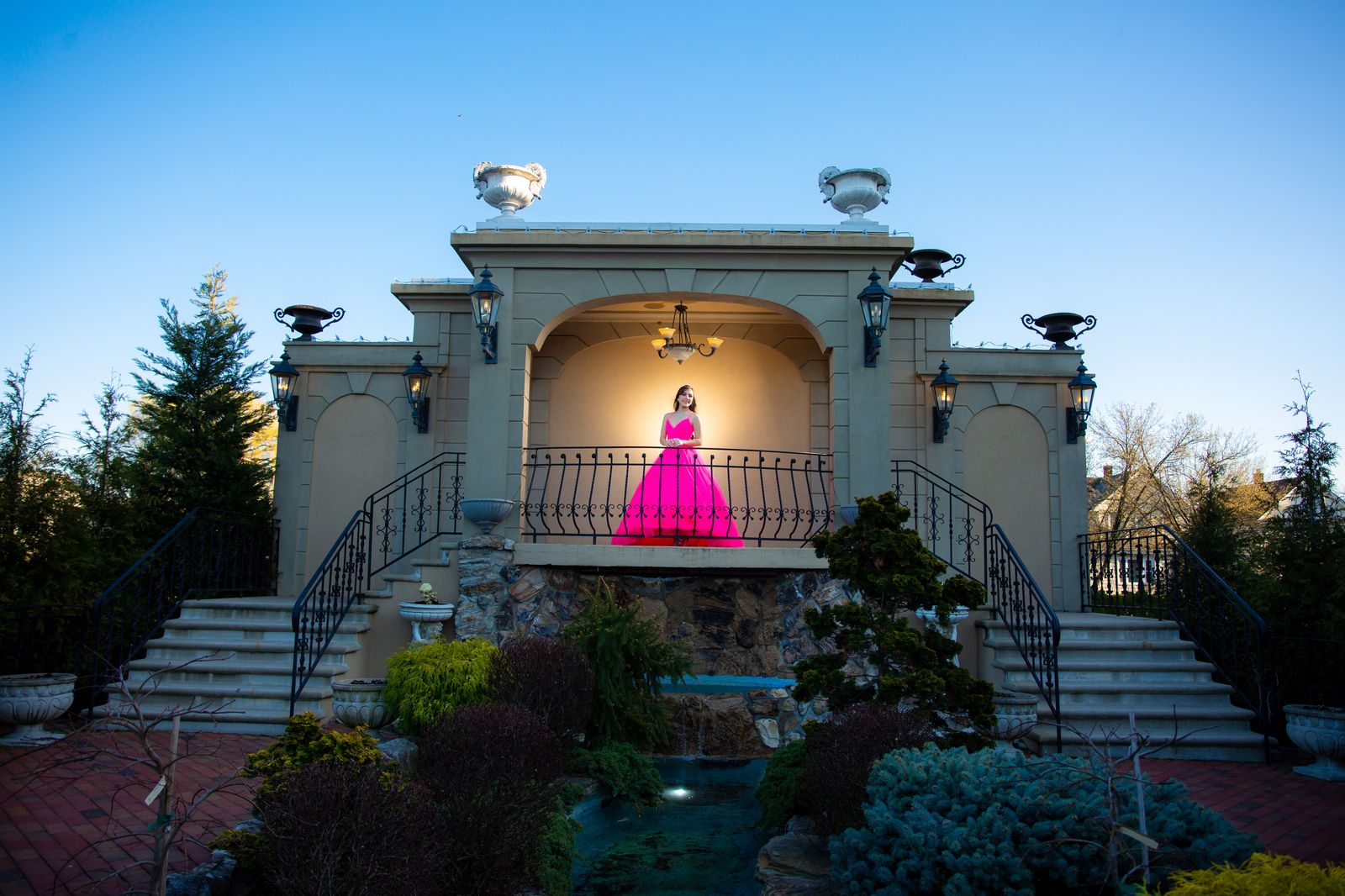 Sweet 16 celebrant in a pink gown on a balcony railing